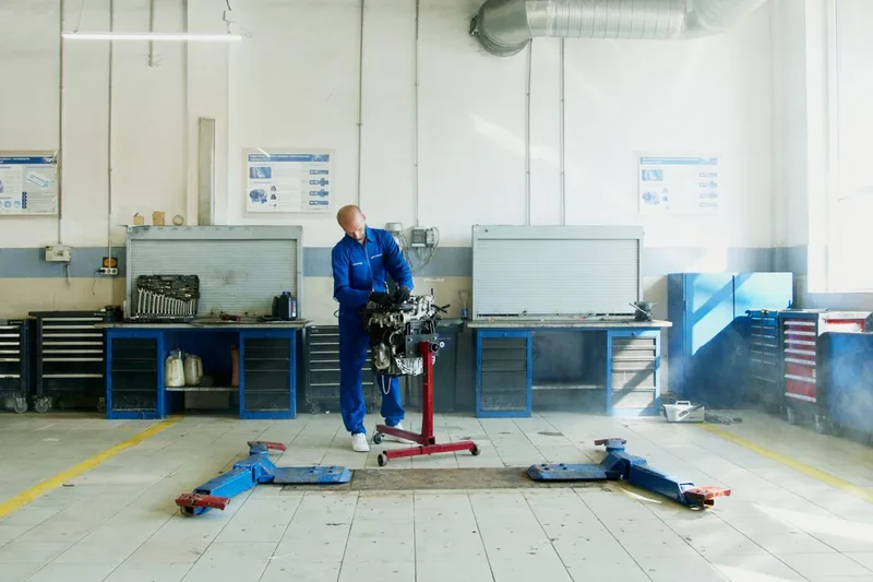 Automotive technician handling an engine in a vehicle repair workshop